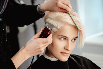 Hairdresser cuts woman client with trimmer. A short haircut, shaved temple and a drawing on the hair.