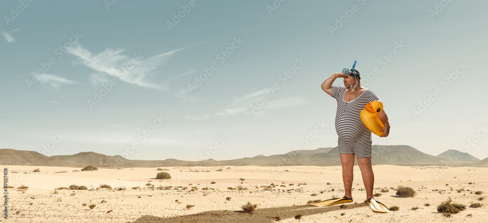 Funny overweight swimmer looking for the beach  in the middle of the desert with copy space - obrazy, fototapety, plakaty 