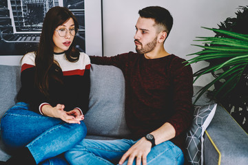 Serious husband and wife concentrated on solving problems of their marriage during leisure time on comfortable sofa in living room, girlfriend and boyfriend have discussion during dispute at home