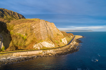 Wall Mural - Northern Ireland, UK. Atlantic coast. Cliffs and Antrim Coast Road, a.k.a. Causeway Costal Route. One of the most scenic coastal roads in Europe. Aerial view near Garron Point in sunrise light