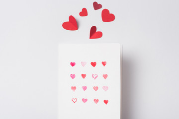 Wall Mural - top view of valentines greeting card and paper red hearts on white background