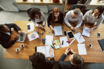 Wall Mural - Top view. Group of young business professionals having a meeting. Diverse group of coworkers discuss new decisions, plans, results, strategy. Creativity, workplace, business, finance, teamwork.