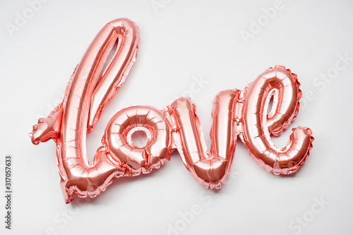 Love word from pink inflatable balloon on white background. The concept of romance, Valentine\'s Day. Love rose gold foil balloon