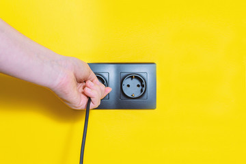 Woman inserts a plug into electric outlet. Black sockets on bright yellow background. Plug and wall socket installation.