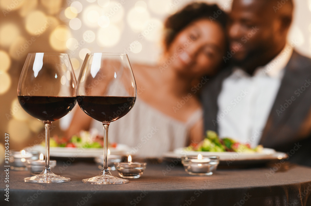 Selective focus on two glasses of wine over cuddling couple - obrazy, fototapety, plakaty 
