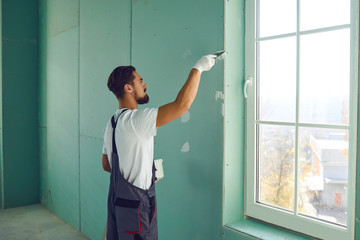 Worker builder plasterer plastering a wall of drywall at a construction site indoors