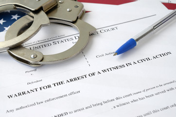 District court warrant for the arrest of a witness in a civil action papers with handcuffs and blue pen on United States flag. Permission to witness arrest