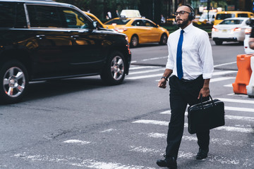 Wall Mural - Confident elegant businessman using headphones while walking on street