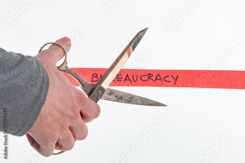 Fotografía Male hand cutting through bureaucracy red tape with scissors isolated on white w