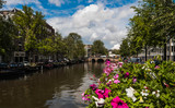 Fototapeta Londyn - Beautiful View of flowers over an Amsterdam canal with a bridge and buildings in the background
