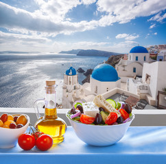 Wall Mural - Greek salad against famous church in Oia village, Santorini island in Greece