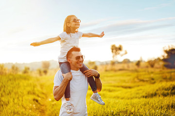 Little girl sitting on father's shoulders and laughing. Summer day, happy family and summer lifestyle concept. Copy space for text.