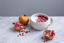 Pomegranate Seeds And Yoghurt In A White Ceramic Bowl On A Marble Table