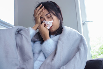 Woman is ill with headache, high fever and flu, sitting under a blanket