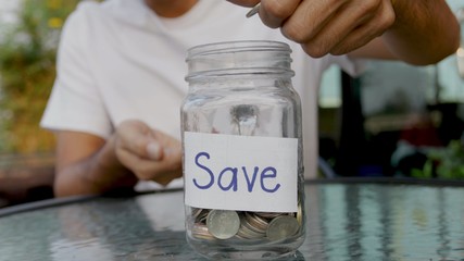 Man putting the coin into a clear glass jar ,saving money concept