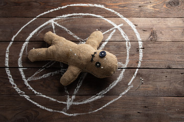 Voodoo doll on a wooden background with dramatic lighting. The concept of witchcraft and black art and the occult. Burlap doll on the background of a drawn star. Stuck pins in the doll.