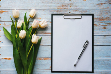 Wall Mural - White bouquet of tulips on wooden blue background with blank paper tablet