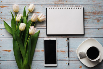 Wall Mural - White bouquet of tulips on wooden background with coffee Cup, smartphone and empty notebook