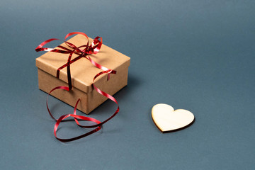 Gift box with red ribbon and a wooden heart on a gray background