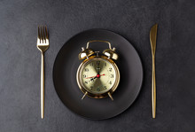Golden Alarm Clock On A Black Plate With A Golden Knife And Fork