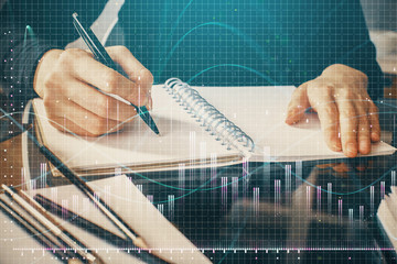 Forex chart hologram on hand taking notes background. Concept of analysis. Multi exposure