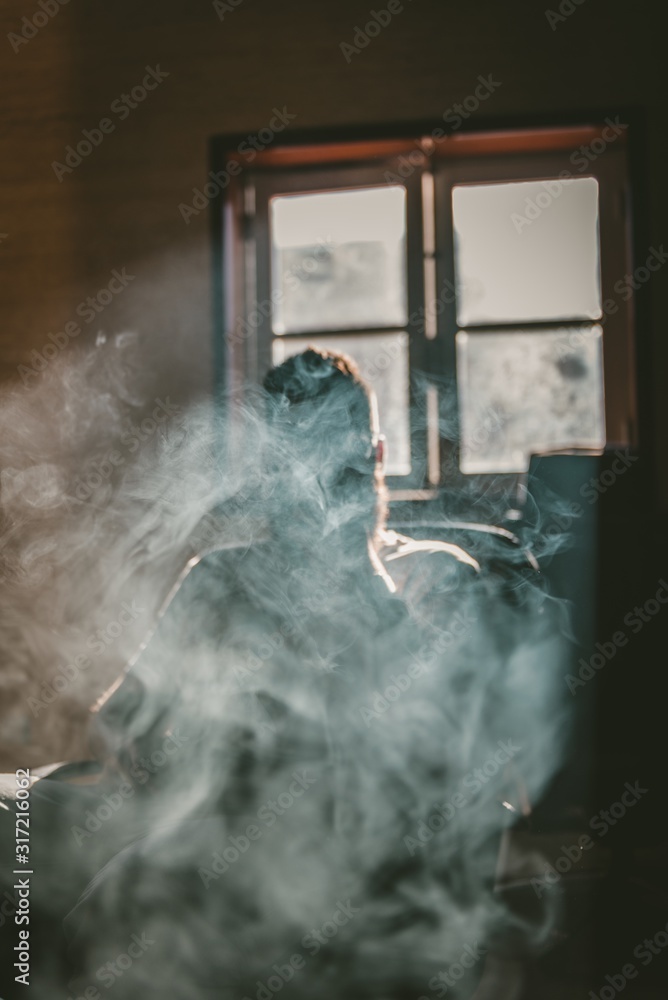 Vertical shot of a person sitting on a chair and smoking filling the room  with smoke Stock Photo