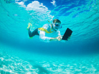 Snorkelling businessman in shirt and tie and matching fins using a tablet computer while swimming under water in tropical turquoise sea