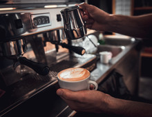 Close Up Of Barista Hands Preparing Cappuccino On Espresso Machine For Customer In Coffee Shop.