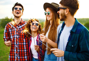 Wall Mural - Group of friends having fun with sparklers sitting on grass in summer park. Teenagers having fun together. Group of young people enjoying party. Rest, fun,  summer, holidays concept.