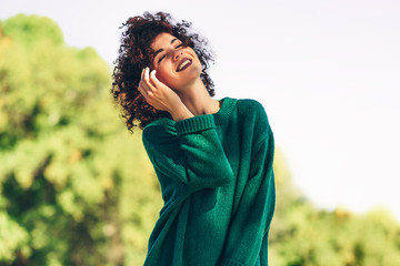 Wall Mural - Image of happy beautiful young woman smiling posing against nature background with windy curly hair, have positive expression, wearing in green sweater. People, travel and lifestyle.