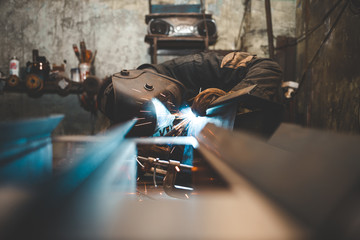 Worker in a welder mask works in a workshop for welding iron. Man makes iron products. Guy works with a welding machine using a mask to protect his eyes from dangerous rays