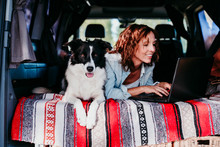 Woman And Border Collie Dog In A Van. Woman Working On Laptop. Travel Concept