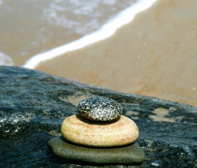 Tower of three wet smooth river stones stacked on wet jetty rock with ocean tide on beach