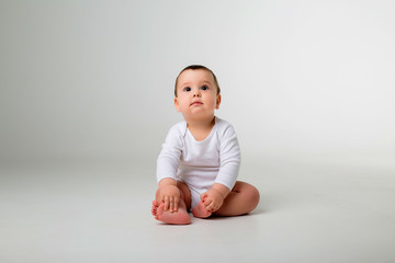 Wall Mural - baby boy 9 months in a white bodysuit sitting on a white background, space for text