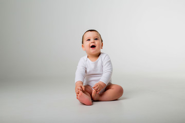 baby boy 9 months in a white bodysuit sitting on a white background, space for text