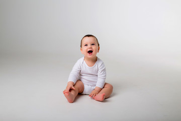 baby boy 9 months in a white bodysuit sitting on a white background, space for text