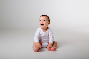 Wall Mural - baby boy 9 months in a white bodysuit sitting on a white background, space for text