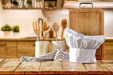 Brown kitchen furniture with empty space on table.Copsy space and kitchen board.White cook hat and few kitchen utensils.Free space for your product and morning time. 