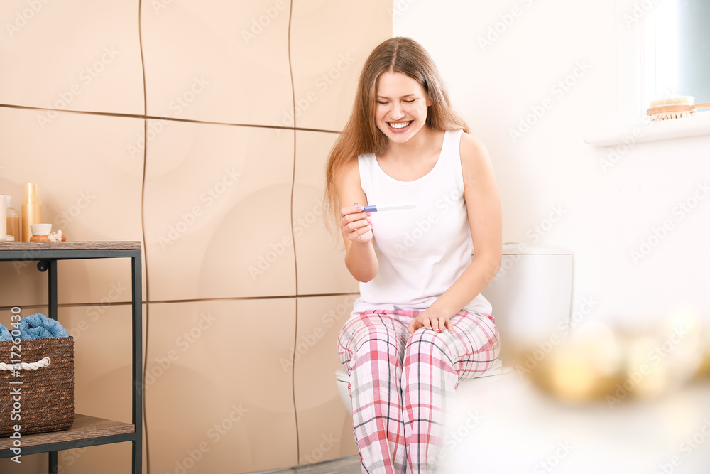 Happy young woman with pregnancy test in bathroom