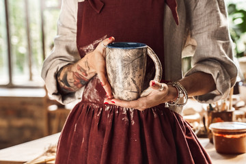 Wall Mural - Craftsperson Concept. Young woman making pottery indoors with beautiful handmade cup close-up posing to camera