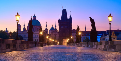 Charles Bridge at dawn, silhouette of Bridge Tower and saint sculptures with street lights in Prague, Czech Republic