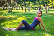 © Михаил Гута - Sporty woman sitting on the grass in the park on the background of trees