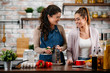 © JustLife - Two friends having fun in kitchen. Sisters cooking together.