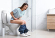 © New Africa - Woman with stomach ache sitting on toilet bowl in bathroom