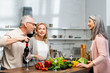 © LIGHTFIELD STUDIOS - smiling woman cooking, man opening bottle with wine and talking with asian woman
