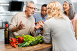 © LIGHTFIELD STUDIOS - smiling multicultural friends talking and standing near table in kitchen
