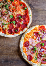 Pepperoni Pizza And Pizza "Four Seasons" With Mozzarella Cheese, Ham, Tomato Sauce, Salami, Bacon, Mushroom, Pepper, Spices And Fresh Basil. Two Italian Pizza On Wooden Table Background