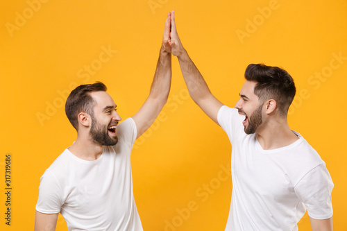 Funny young men guys friends in white blank empty t-shirts posing isolated on yellow orange background in studio Tableau sur Toile