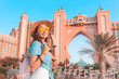 © EdNurg - Happy asian girl traveller relaxing near famous luxury Atlantis hotel building on a Jumeirah Palm Island in Duba, UAE