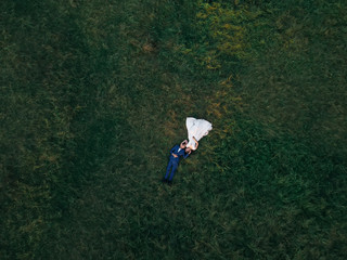 top view of newlyweds are lying on the grass and looking at each